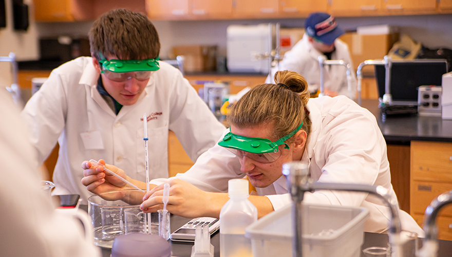 Male students in safety goggles working in a lab