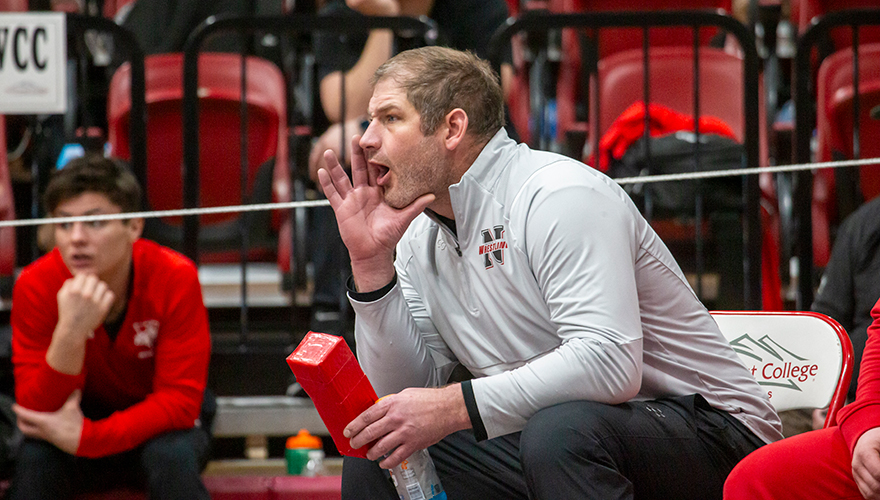 Assistant wrestling coach seated in a folding chair yelling encouragement with fans in the background