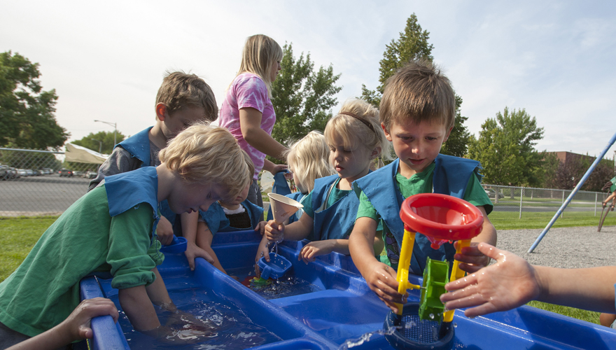 Children playing outside with toys in a plastic water-filled basin with partitions