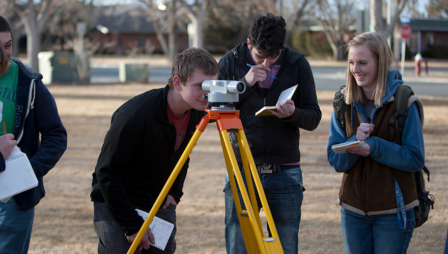 Students outside Science and Math Building on campus doing surveying work