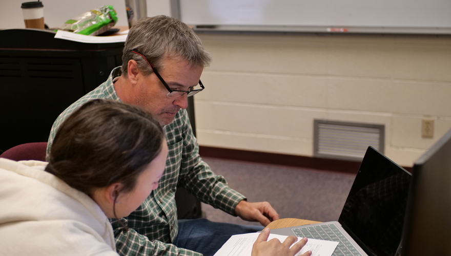 Male professor in glasses helping a student working on a laptop