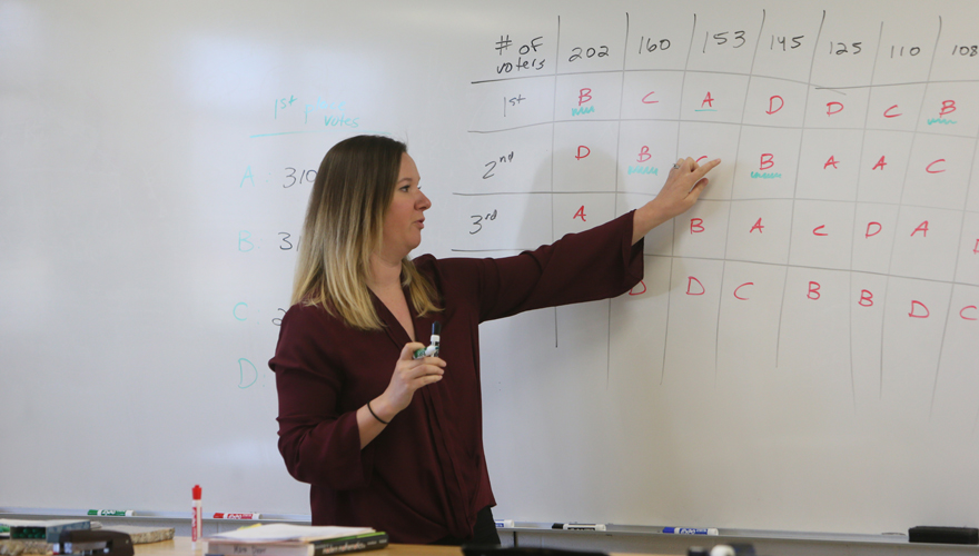 Female instructor pointing to mathematics table on a white board