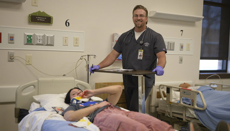 Male nursing student standing next to a bed with a patient in a neckbrace