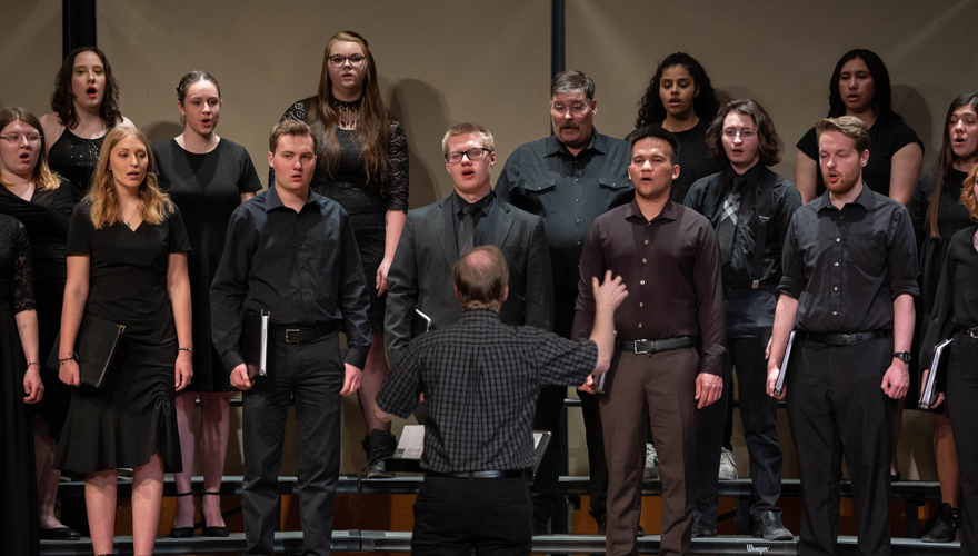 A choir dressed in all black sings in front of their director