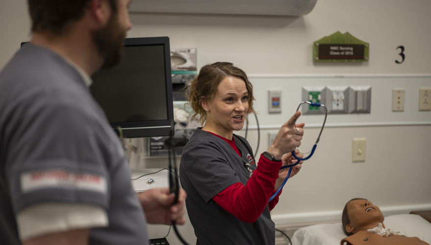 Female nursing instructor pointing toward students next to a hospital bed