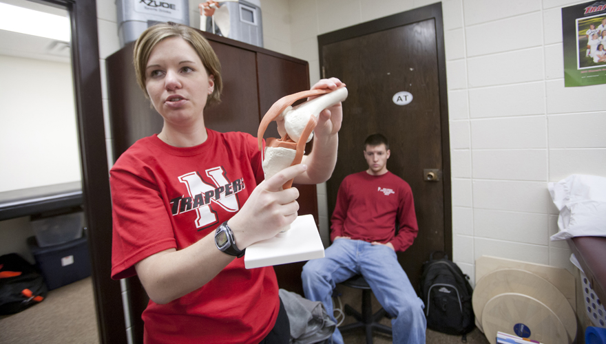 Instructor in red Northwest College Trappers shirt holding a plastic model of a knee