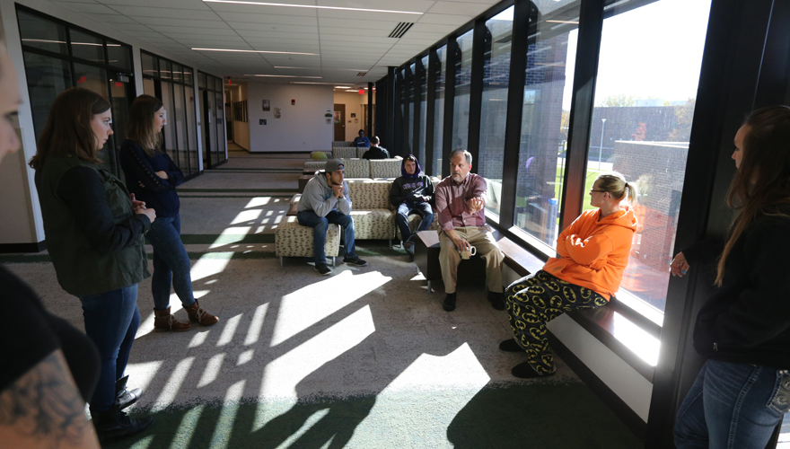 Students sitting and standing in a sunny lobby talking with a Northwest College professor