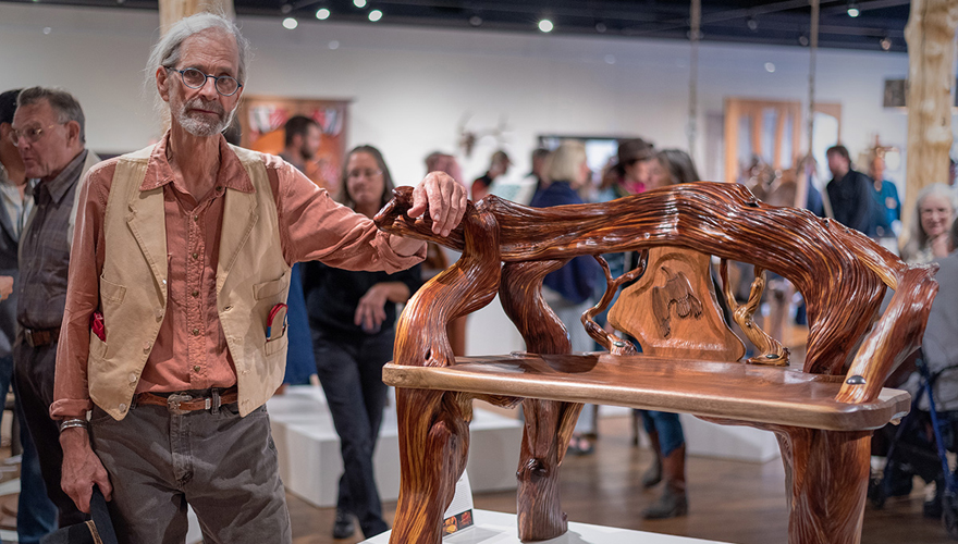 Older man in an art gallery leaning on his hand carved wooden bench