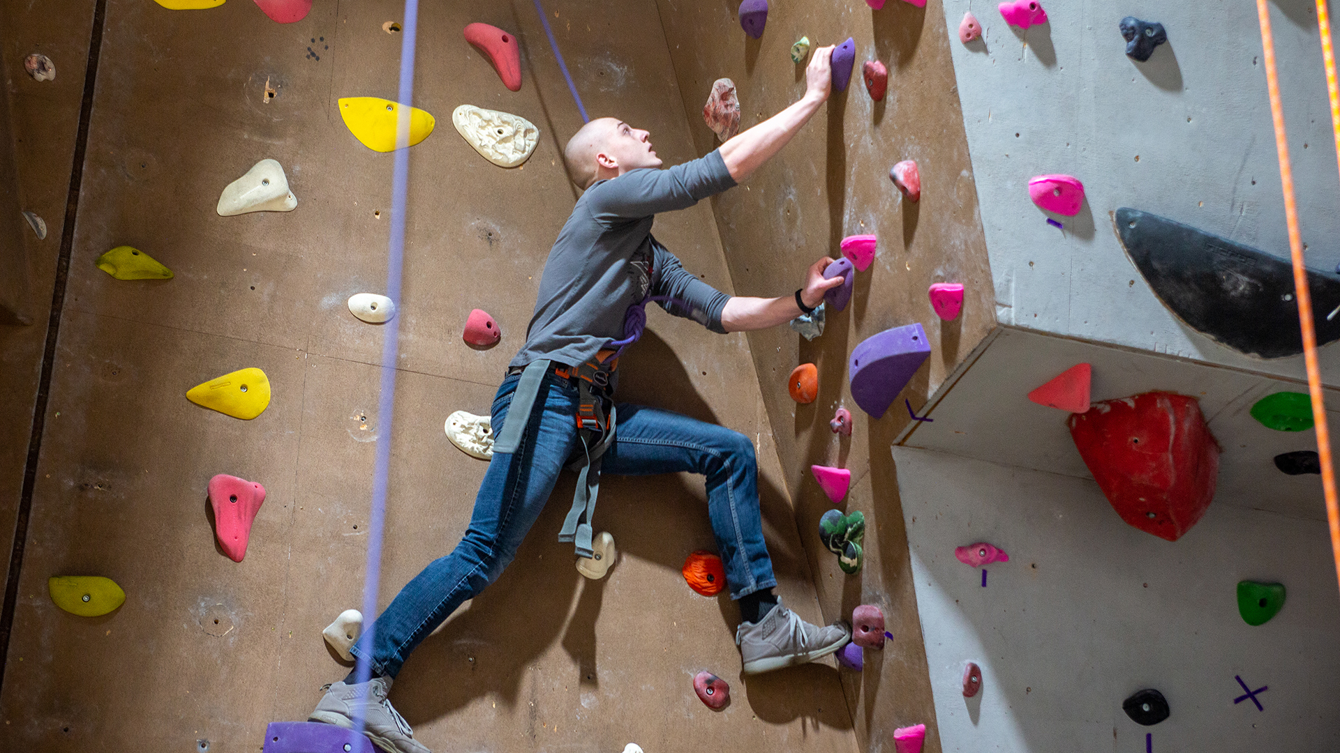 Male student climbing up a climbing wall using handgrips