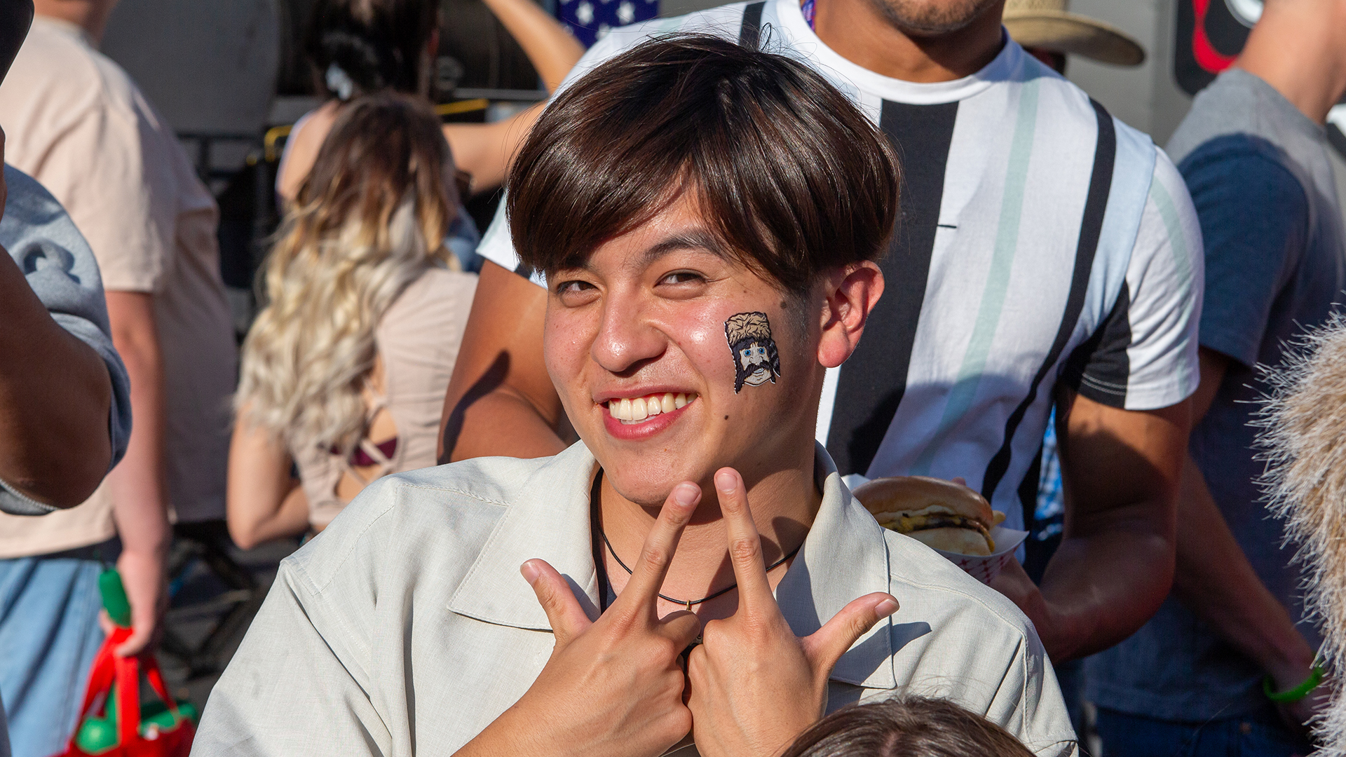 Smiling male student pointing to a Trapper tattoo on his face