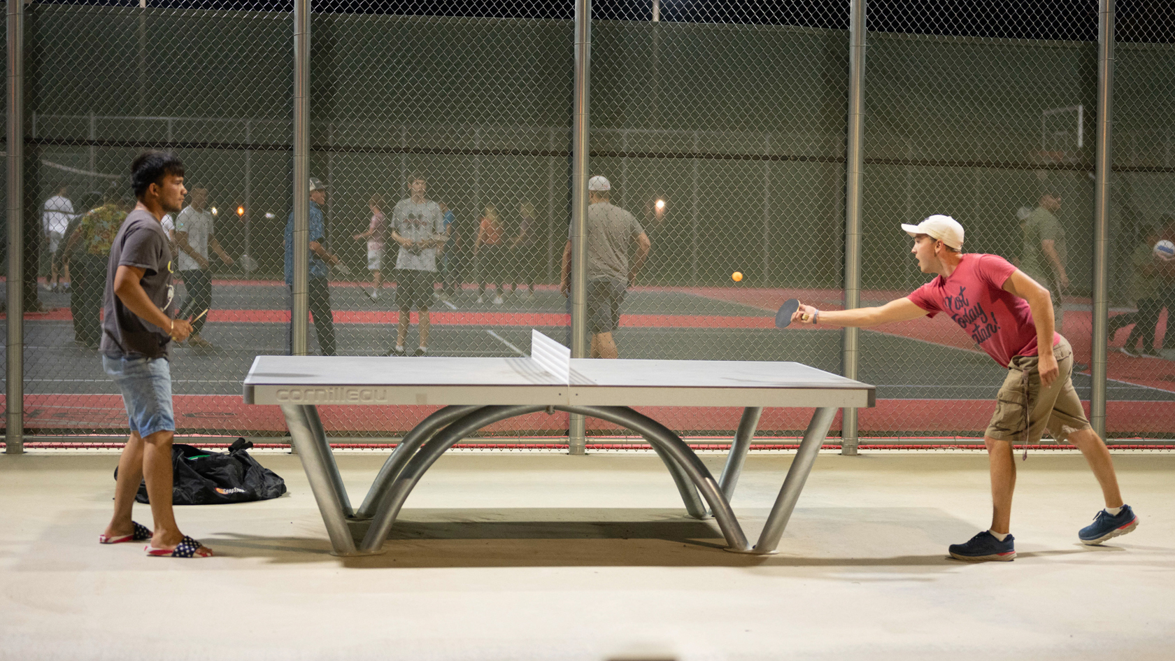 Male students playing ping pong on an outdoor court at night