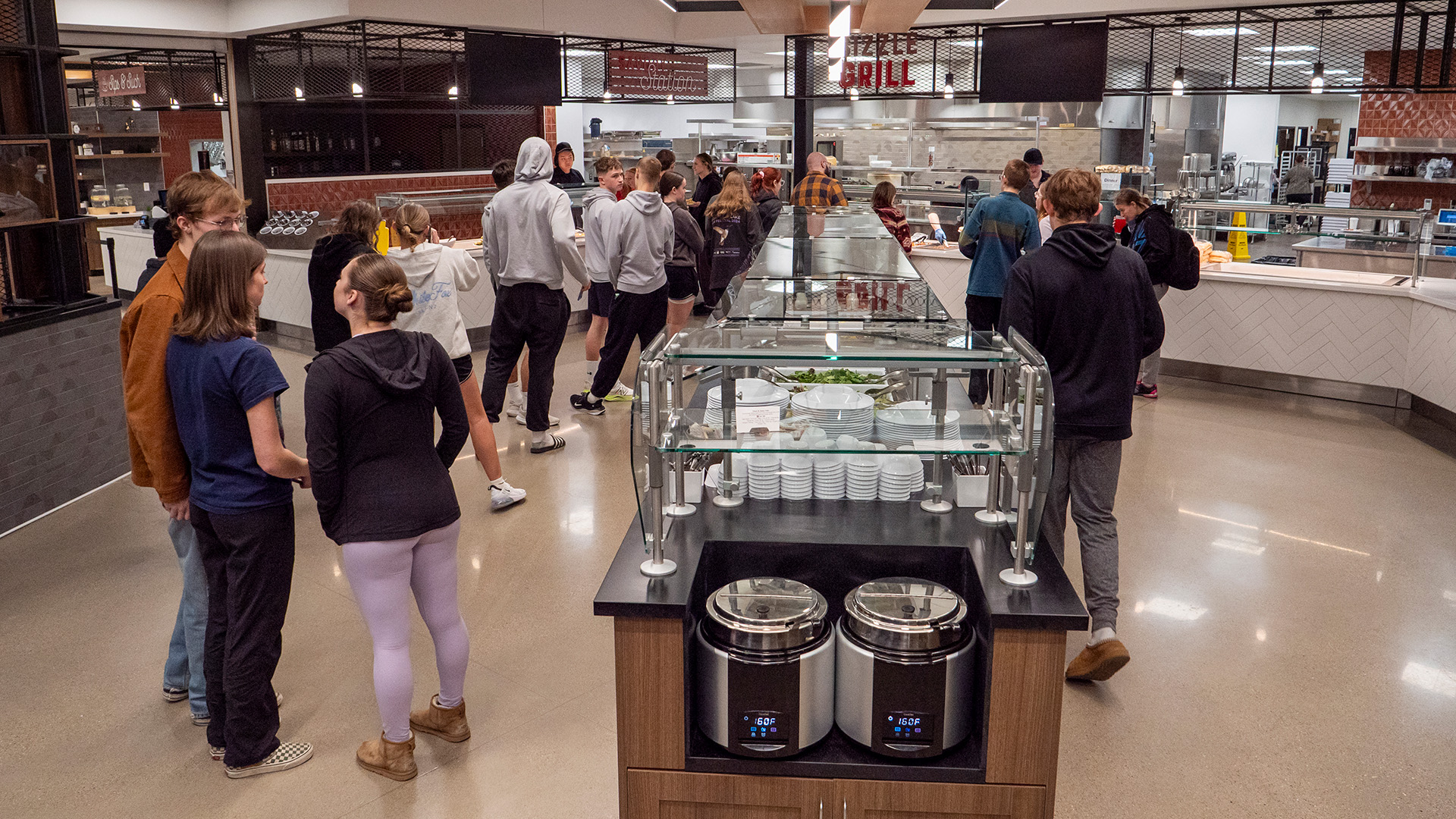 Students standing in line for dinner on either side of a salad bar