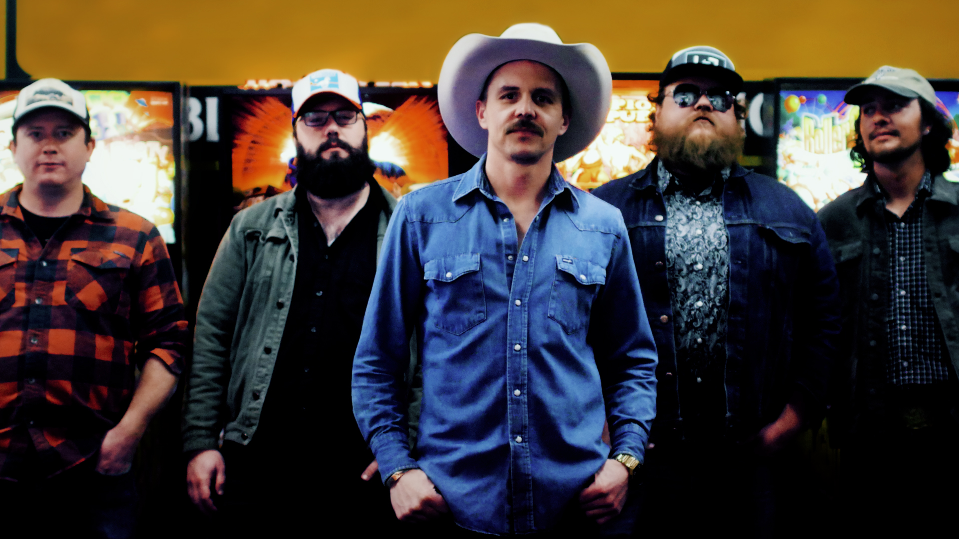 Kalyn Beasley in a blue short and cowboy hat standing in front of his four bandmates, two on each side, all wearing baseball caps