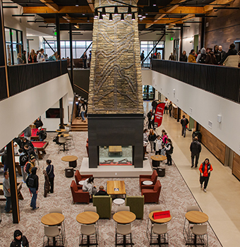 Second floor view of floor to ceiling fireplace with artwork on stone, all surrounded by talking people walking and sitting